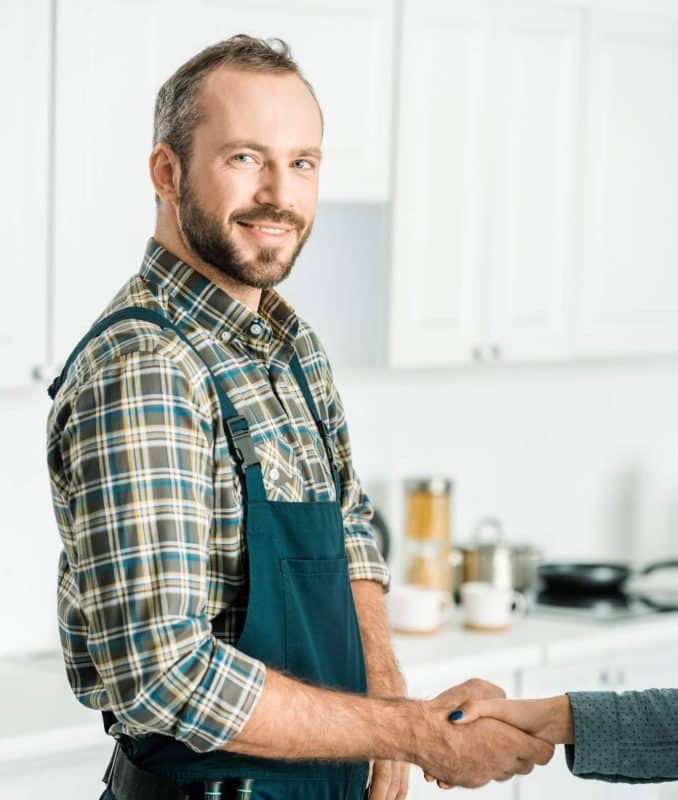 smiling handsome plumber and customer shaking hands in kitchen