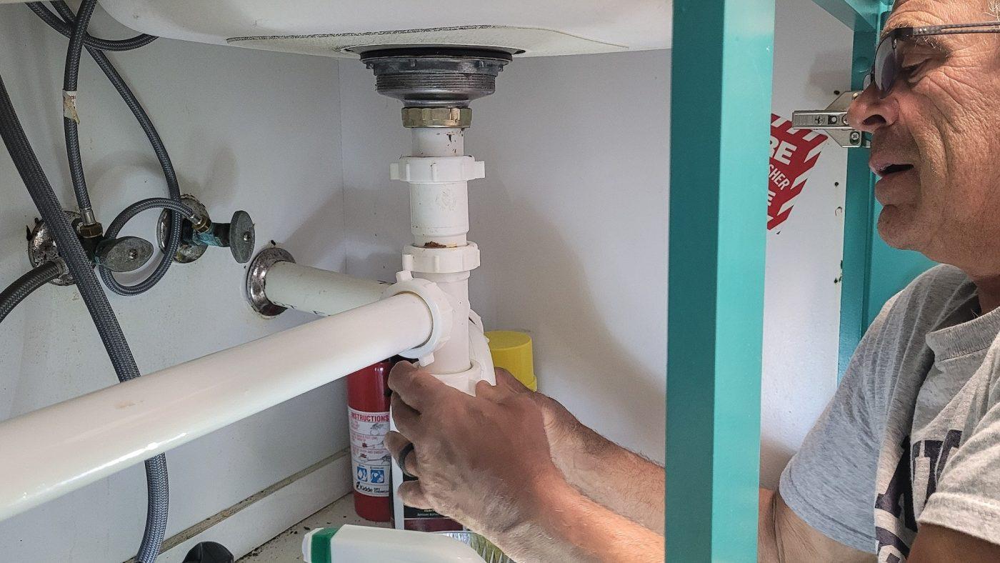 Professional Plumber working on kitchen utilities under sink stopping a water leak in repairs.