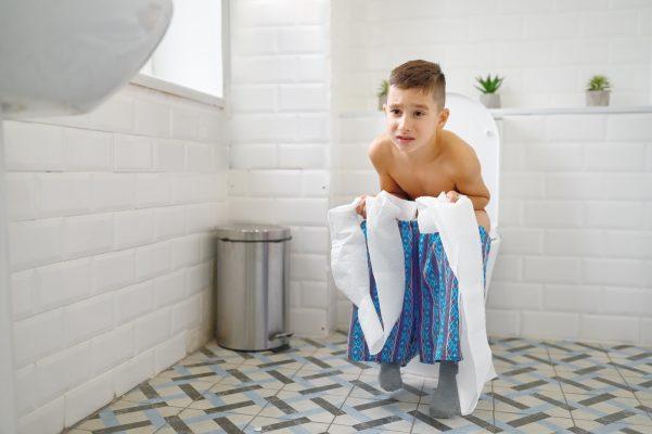 Frowning little boy sitting on toilet trying to poop