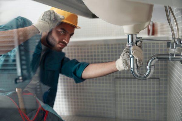 Male plumber is repairing faucet of a sink at bathroom. Good quality plumbing company service