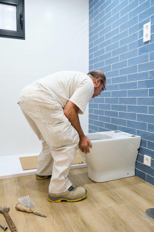 Senior plumber installer installing toilet.